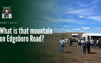 What Is That Mountain on Edgeboro Road? A group of about a dozen visitors stands on bare graded ground at the Edgeboro Road landfill beside two white shuttle buses, under a blue sky with scattered clouds. Overlaid title card reads: Eyes on EB, Part 1 of 4, What is that mountain on Edgeboro Road?