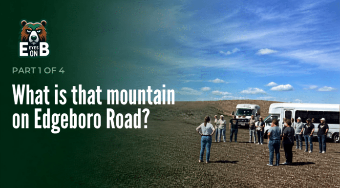 What Is That Mountain on Edgeboro Road? A group of about a dozen visitors stands on bare graded ground at the Edgeboro Road landfill beside two white shuttle buses, under a blue sky with scattered clouds. Overlaid title card reads: Eyes on EB, Part 1 of 4, What is that mountain on Edgeboro Road?